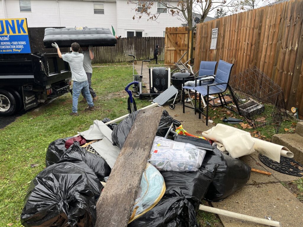 Employees loading an inflatable mattress into a truck, with a large pile of junk in the foreground for Lug Stars Junk Removal in Columbus, OH.