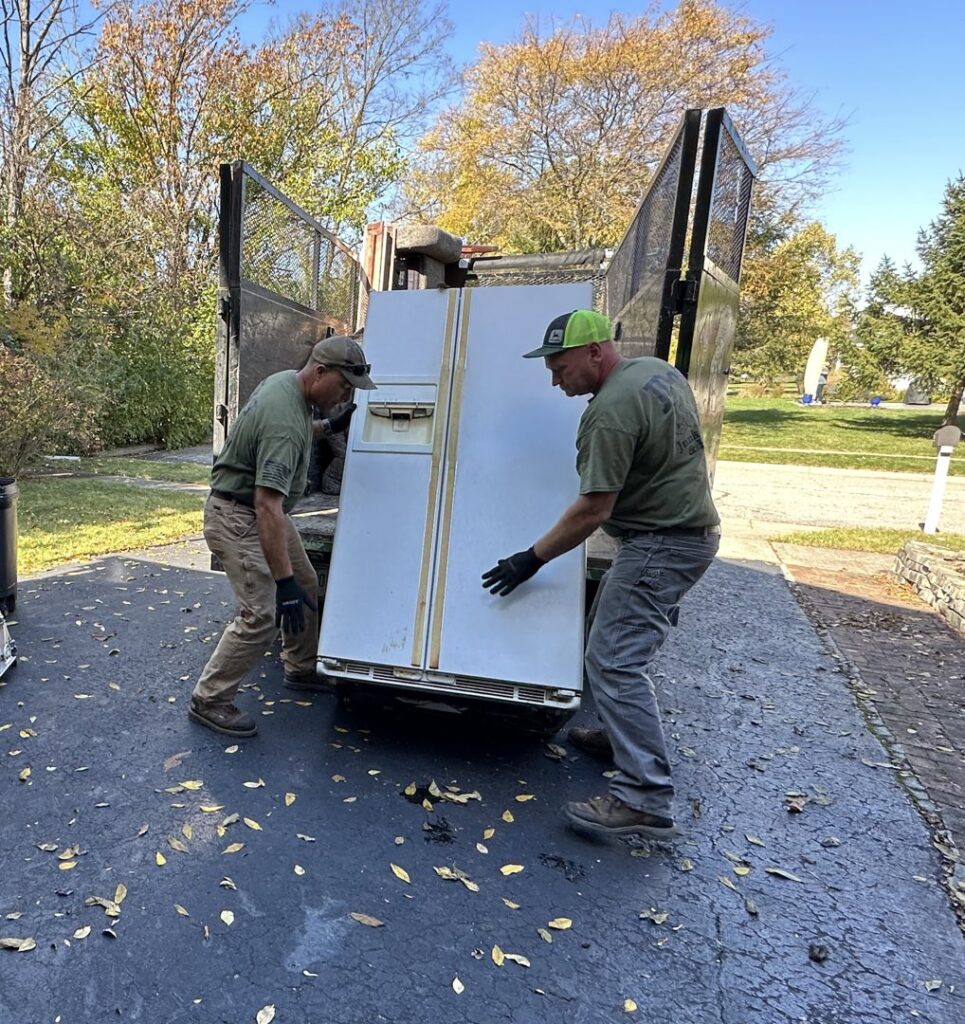 Two JDog Junk Removal & Hauling employees loading a large white refrigerator onto a trailer in Columbus, OH.