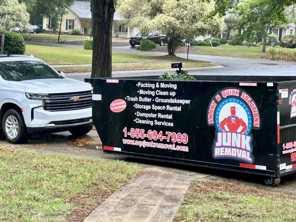 An empty SQS Junk Removal dumpster being loaded onto a truck in Charlotte, NC, for a junk removal service.