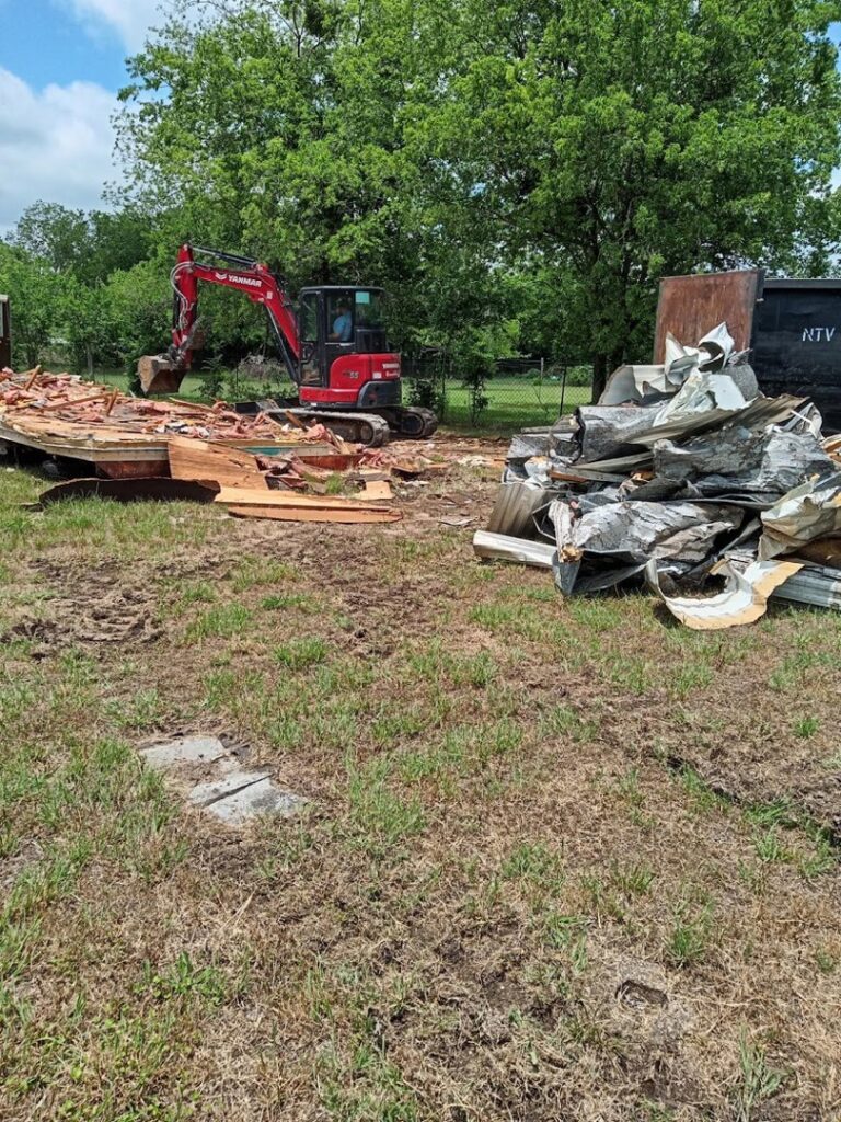 An excavator from Green Source Junk Removal clearing demolition debris from a large outdoor area in Fort Worth, TX.