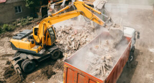 An excavator loading demolition debris into a dump truck, showcasing a junk removal job by Epic Junk Removal SD in San Diego, CA.