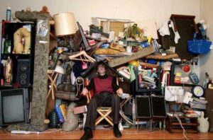 A man sitting in a room overwhelmed by extreme clutter and junk, illustrating a hoarding cleanup service offered by IHaul Austin in Austin, TX.