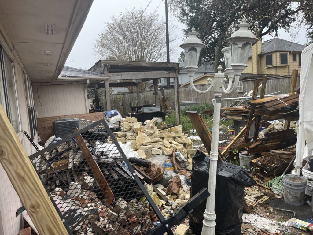 A very cluttered backyard with bricks, metal, wood, and trash, showing a major junk removal project by Duane's junk removal LLC in Houston, TX.