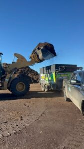 A front-end loader dumping landscaping debris into a Haul Away Any Day trailer in San Diego, CA.