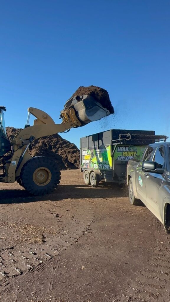 A front-end loader dumping landscaping debris into a Haul Away Any Day trailer in San Diego, CA.