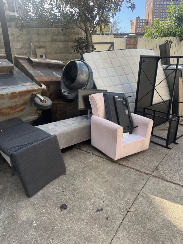 A large pile of discarded furniture, a mattress, and a television next to a dumpster, awaiting removal by HustleTown Junk Removal in Houston, TX.
