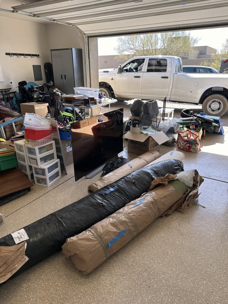 A garage filled with rolled carpets, boxes, and various items awaiting junk removal by North Valley Junk Removal in Phoenix, AZ.