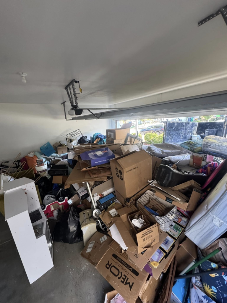 A cluttered garage filled with boxes, furniture, and various junk items before removal by Junkjet in Charlotte, NC.