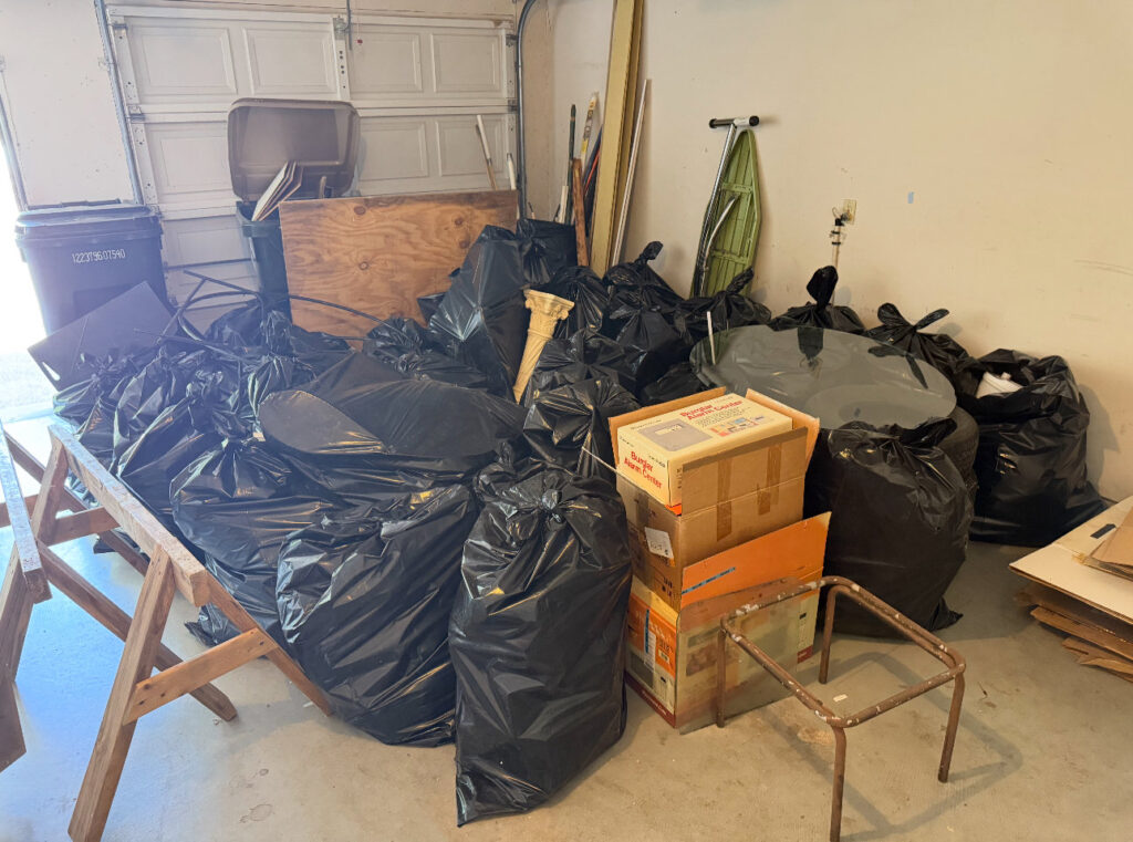 A garage filled with numerous black trash bags and boxes, indicating a large junk removal job for Junk Out Boyz LLC in Austin, TX.