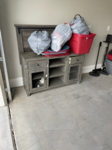 A TV stand with trash bags and other items in a garage, awaiting junk removal by Cee J Junk Removal LLC in Phoenix, AZ.