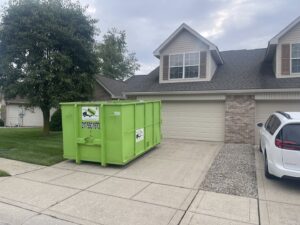 A bright green Bin There Dump That dumpster placed on a residential driveway for junk removal in Indianapolis, IN.