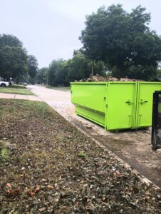 A large green dumpster from Herrera Hauling & Junk Removal on a residential street, ready for yard debris in Fort Worth, TX.