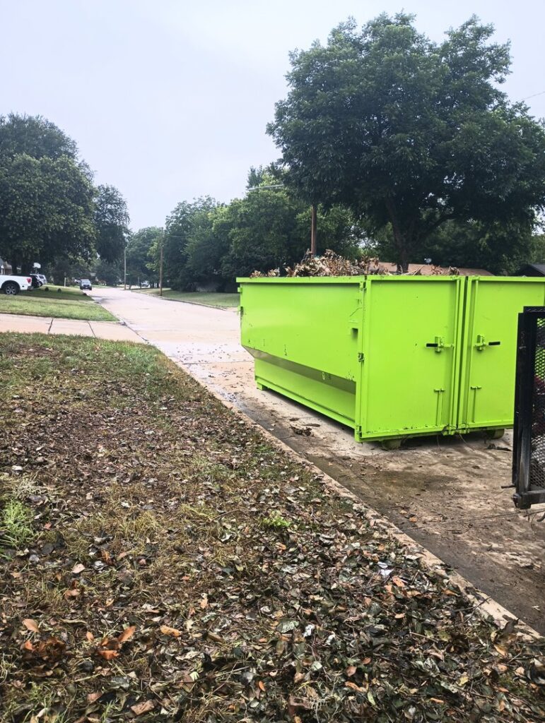 A large green dumpster from Herrera Hauling & Junk Removal on a residential street, ready for yard debris in Fort Worth, TX.