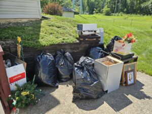 Household junk, including black trash bags and cardboard boxes, piled outside a residence for removal by Purefoy's Professionals in Columbus, OH.