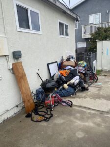 A pile of miscellaneous household junk, including a grill and bicycle, next to a house for Crisan Junk Removal in San Diego, CA.