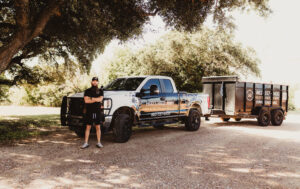 A Hud's Haul Away Junk Removal & Demolition branded truck and empty trailer ready for service in Fort Worth, TX.