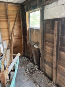 An interior room with exposed wooden walls and construction debris on the floor, showing a renovation or demolition cleanup by Jacksonville Hauling & Junk Removal in Jacksonville, FL.