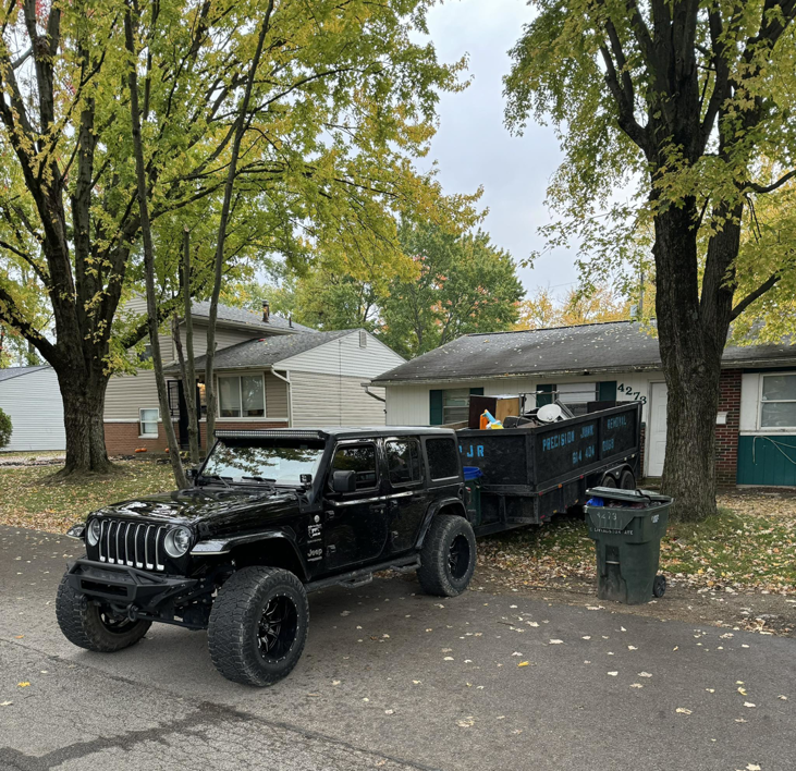 A black Jeep pulling a junk removal trailer filled with items for Precision Junk Removal in Columbus, OH.