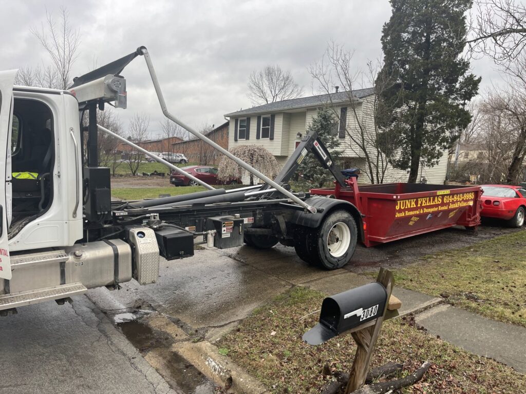 A Junk Fellas LLC truck deploying a red dumpster in a residential driveway for junk removal in Columbus, OH.