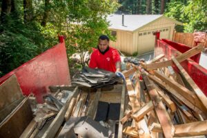 A Junk King employee loading roofing shingles and wood debris into a junk removal truck in Austin, TX
