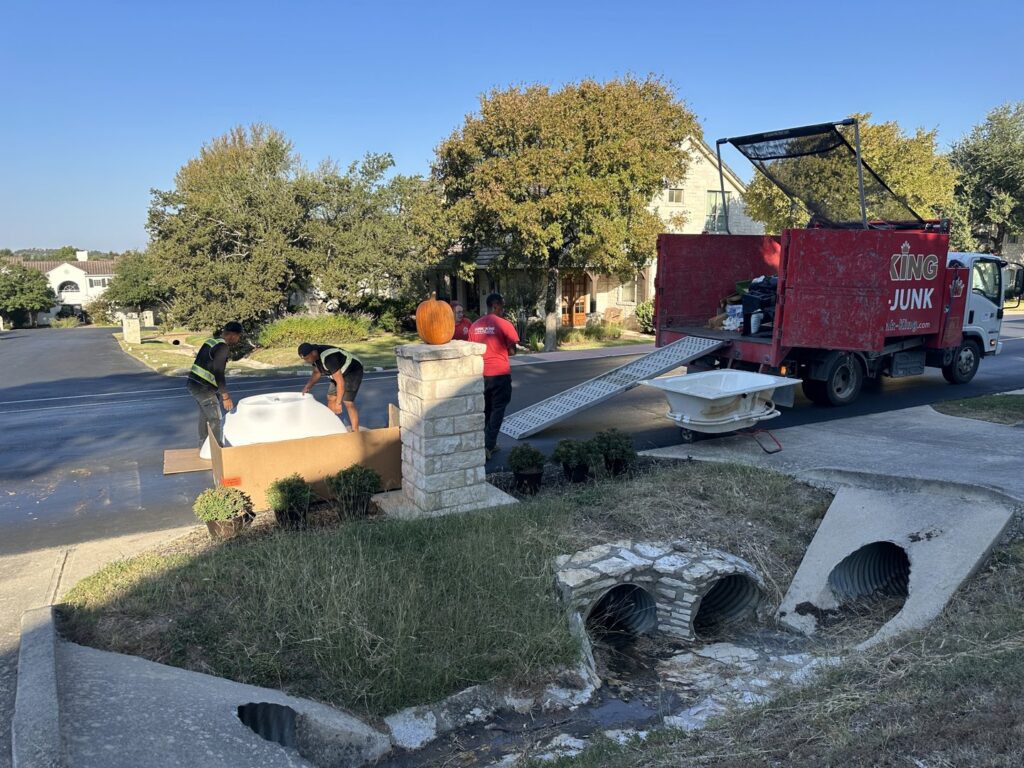 Junk King employees loading a large white item onto a ramp leading to their junk removal truck in Austin, TX