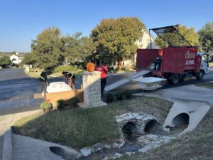 Junk King employees loading a large white item onto a ramp leading to their junk removal truck in Austin, TX