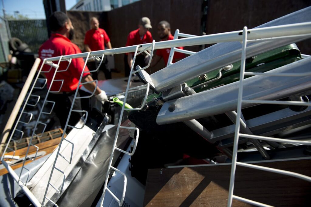 Junk King employees loading metal items like a ladder and shelving into a junk removal truck in Austin, TX
