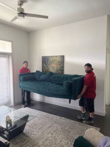 Two Junk King employees carefully removing a green couch from a home in Austin, TX