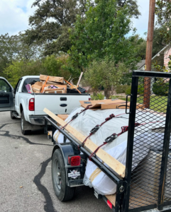 A white pickup truck and trailer loaded with various items for removal by JT Junk Solutions in Austin, TX.