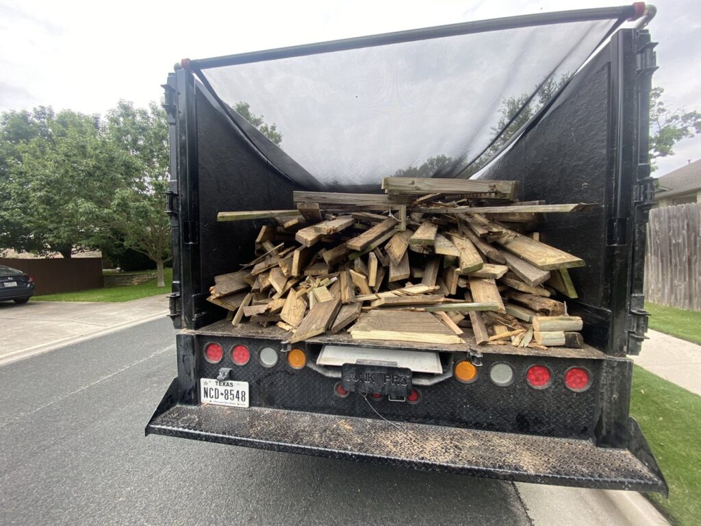 A pile of household junk and debris on a driveway with a 1-800-JUNKPRO truck in the background in Austin, TX.