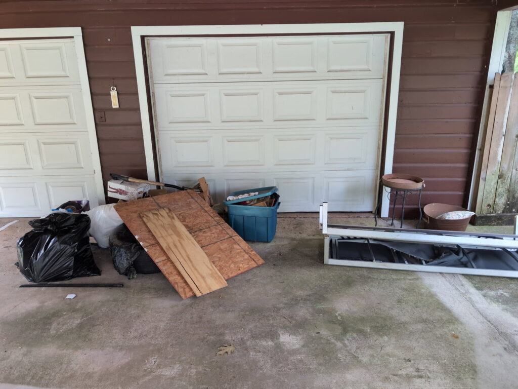Household junk and construction debris piled outside a garage, ready for removal by Clutch City Junk Removal in Tomball, TX.