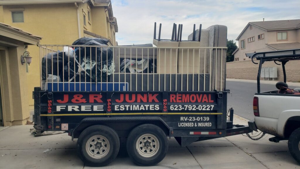 A branded J & R Junk Removal trailer filled with various household junk and debris in Phoenix, AZ, ready for hauling.