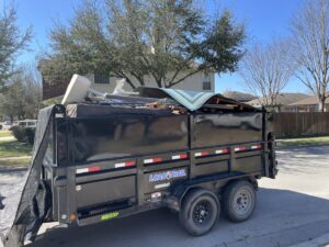 A junk removal trailer filled with various debris and furniture on a residential street by Firefighter Junk Removal in Austin, TX.