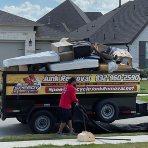 A Speedy Junk Removal & recycling team member sweeping around a trailer full of household junk in Houston, TX.