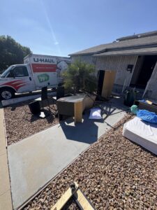A white pickup truck towing a branded junk removal trailer through an alley for Priority Hauling and Junk Removal San Diego, CA.
