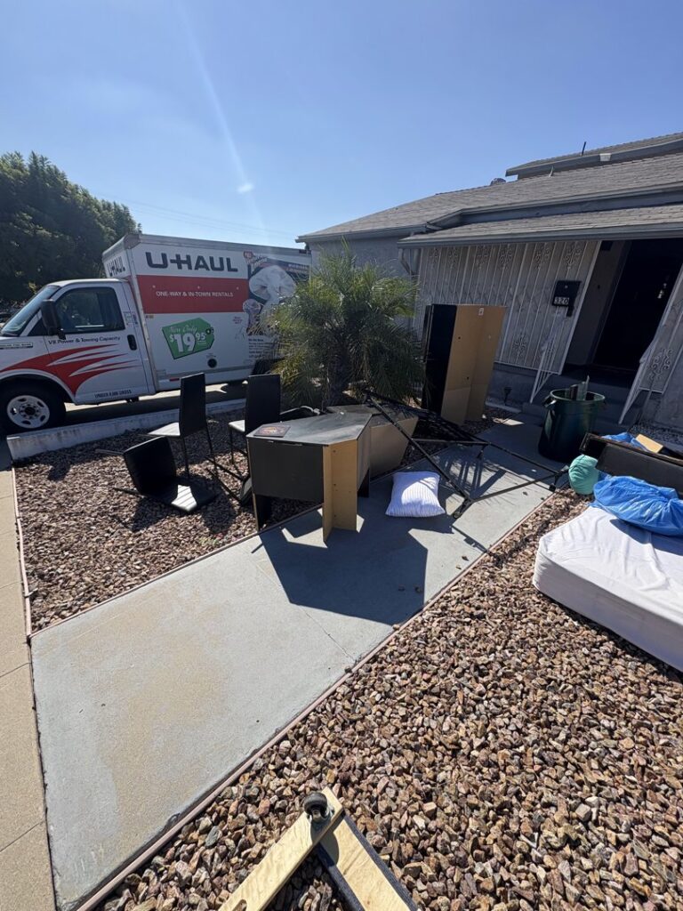 A white pickup truck towing a branded junk removal trailer through an alley for Priority Hauling and Junk Removal San Diego, CA.
