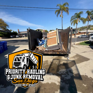 A branded junk removal trailer parked with couch cushions on the ground nearby, ready for pickup by Priority Hauling and Junk Removal San Diego, CA.