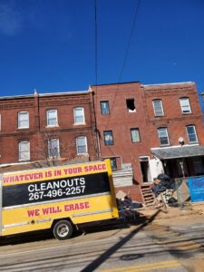A Space Erasers Junk Removal truck parked at a residential cleanout job site with debris outside in Philadelphia, PA