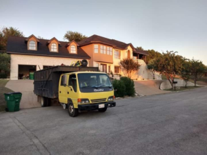 A yellow DonkeyJunk Removal and Home Services truck with a full dumpster bed parked in front of a residential home in Austin, TX