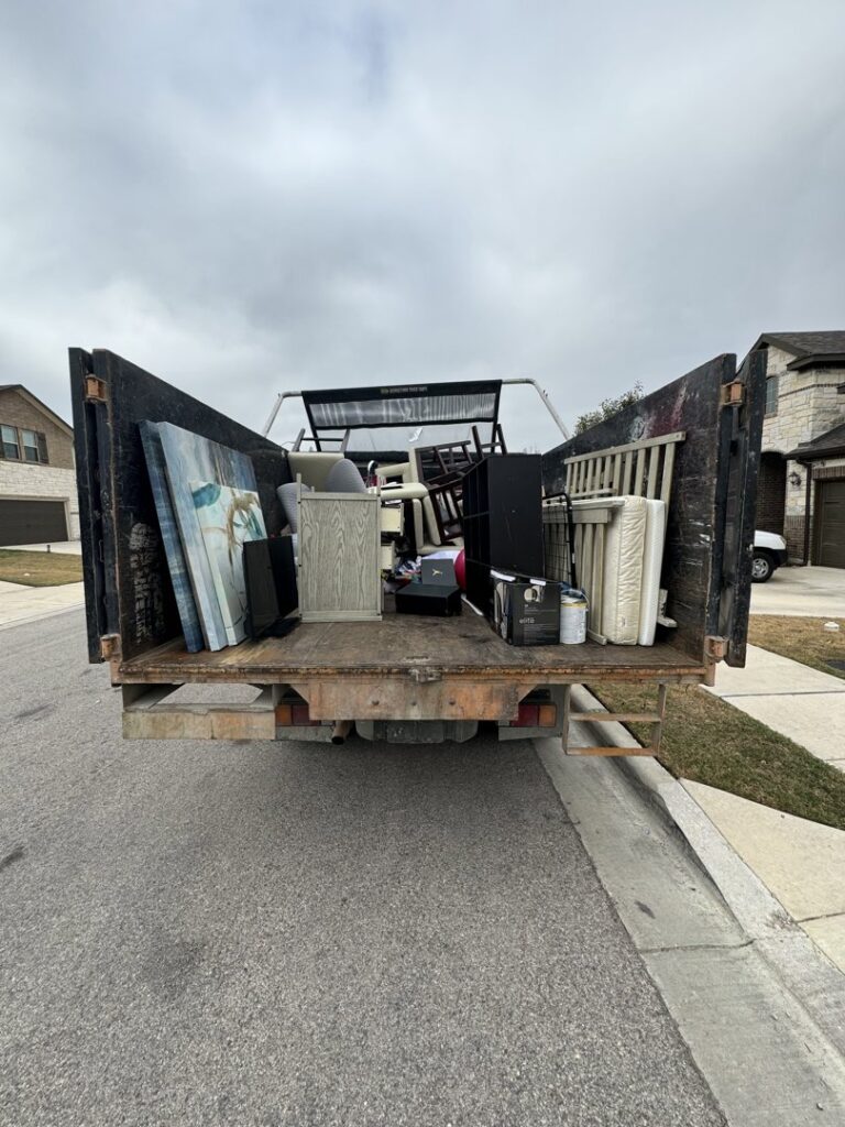 The back of a Junk Out Boyz LLC truck loaded with various household items and debris after a junk removal service in Austin, TX.