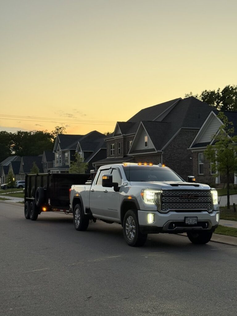 A white pickup truck and dump trailer parked on a residential street at sunset by Junkjet in Charlotte, NC.