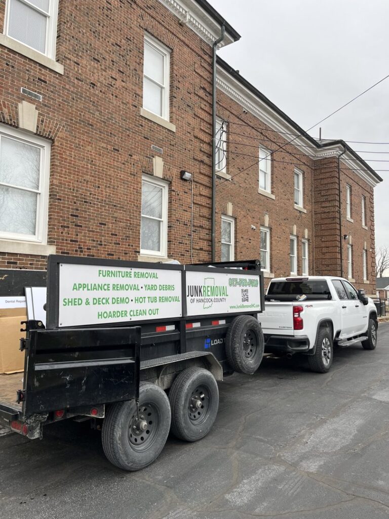 A Junk Removal of Hancock County truck and trailer parked next to a brick building, ready for service in Indianapolis, IN.