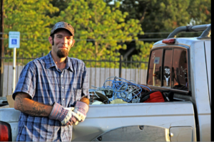 A Smiley's Junk Removal & Recycling worker in Austin, TX, standing by a truck bed filled with wires and other items for removal.