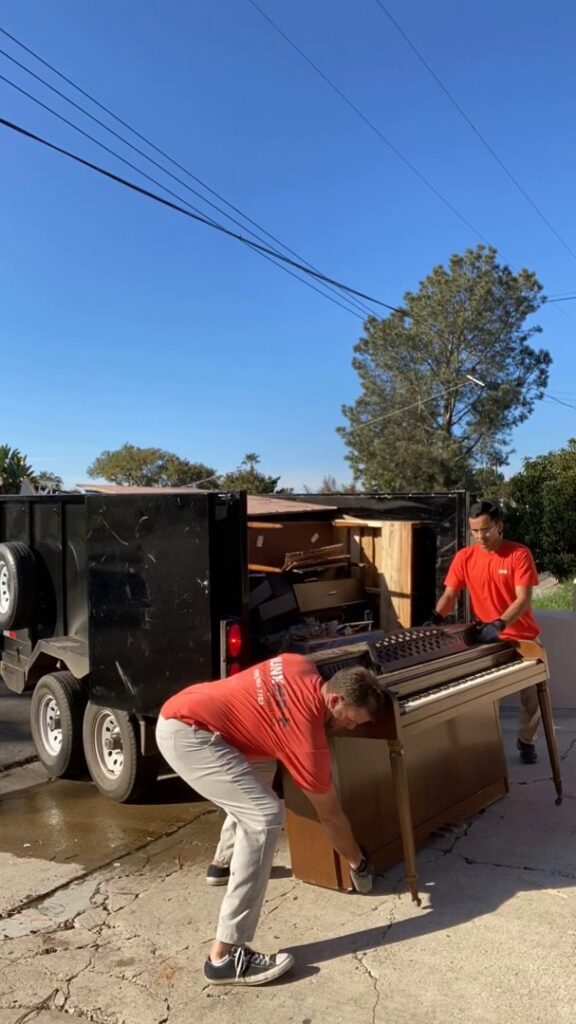 JunkMD team members carefully removing a heavy piano onto a trailer in San Diego, CA.
