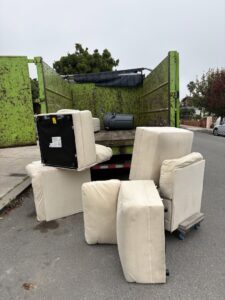 JunkMD truck loading multiple upholstered furniture pieces from a street in San Diego, CA.