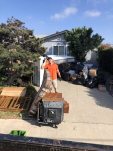 A JunkMD worker standing in a driveway with a large pile of household junk ready for removal in San Diego, CA.