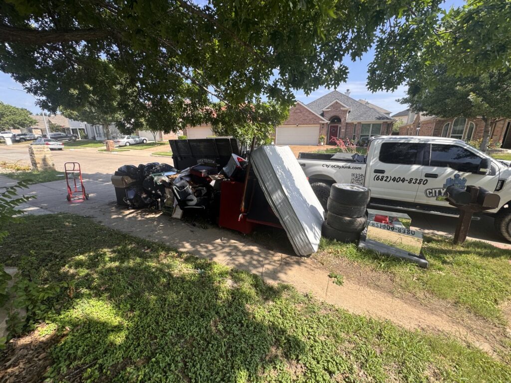 A large curbside pile of junk, including a mattress and tires, with a City to City Junk Removal truck in Fort Worth, TX.