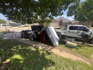 A large curbside pile of junk, including a mattress and tires, with a City to City Junk Removal truck in Fort Worth, TX.