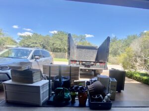 A large pile of junk, including a TV, bicycles, and trash bags, on a grassy area next to a sidewalk in Austin, TX.