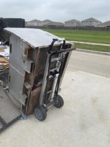 A large, old metal unit being moved with a dolly, ready for removal by HustleTown Junk Removal in Houston, TX.